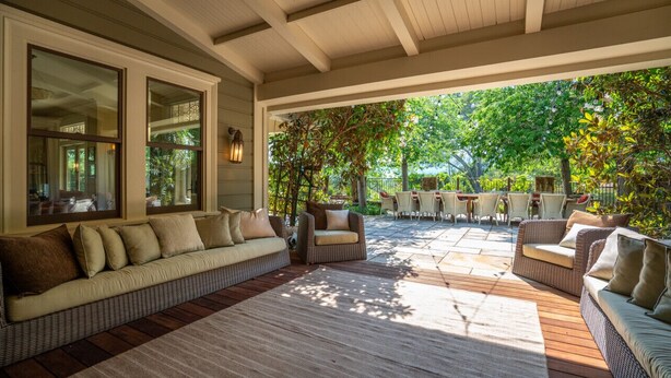 Ein überdachter Patio-Bereich mit Rattanmöbeln, darunter eine Couch und Stühle, sowie ein Esstisch für vier Personen.