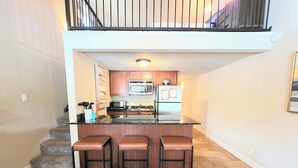 A kitchen with a central island, three bar stools, a microwave, a refrigerator, and a staircase leading to a balcony. - Better to WAKE at the LAKE (Hot Springs)