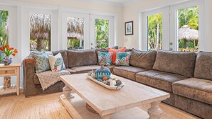 A cozy living room with a large sectional sofa, a wooden coffee table, and a view of lush greenery through large windows. - Kon-Tiki Falls: Jupiter`s Exclusive Private Resort! (Jupiter)