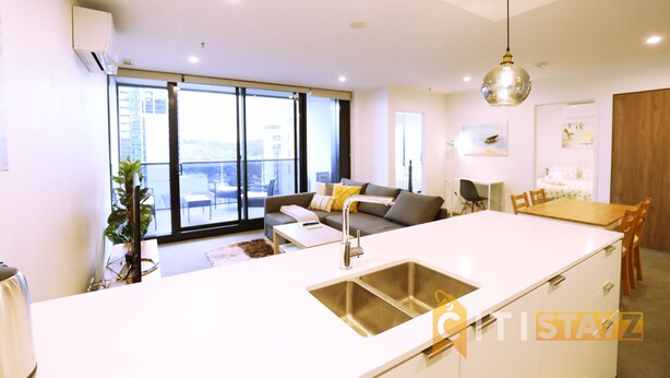 A modern apartment with a kitchen island, dining area, and a living room with a sofa and large windows. - 2bd 2bth - Chic Apt in Woden CBD (Phillip)