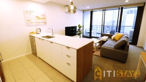 A modern kitchen with a central island, a dining area with a sofa and table, and large windows offering a city view. - 2bd 2bth - Chic Apt in Woden CBD (Phillip)