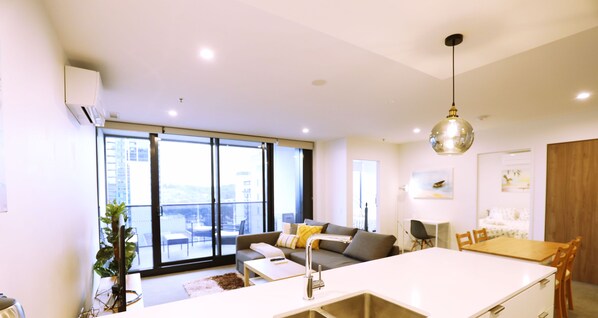 A modern apartment with a kitchen island, dining area, and a living room with a sofa and large windows.