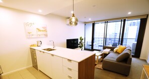 A modern kitchen with a central island, a dining area with a sofa and table, and large windows offering a city view.