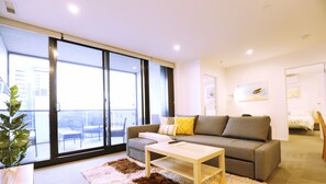 A modern living room with a sofa, a coffee table, and a large window offering a view of the city.