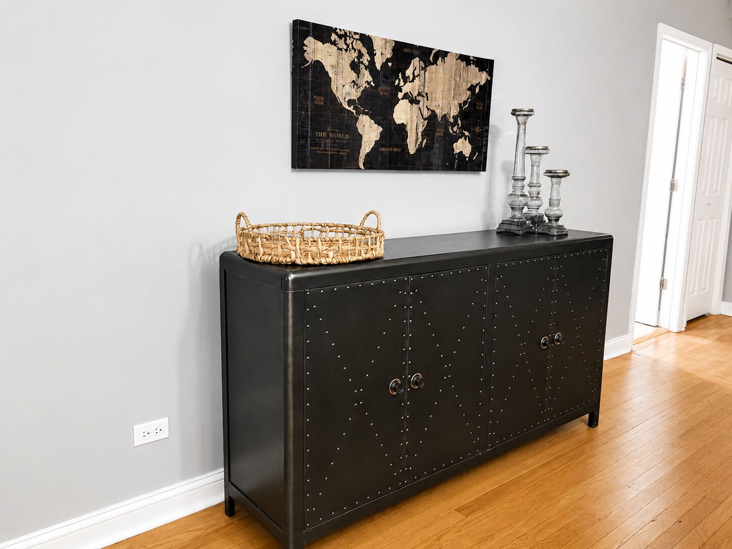 Un meuble métallique noir avec un panier tressé posé sur le dessus, une carte du monde accrochée au mur et une porte visible au fond.