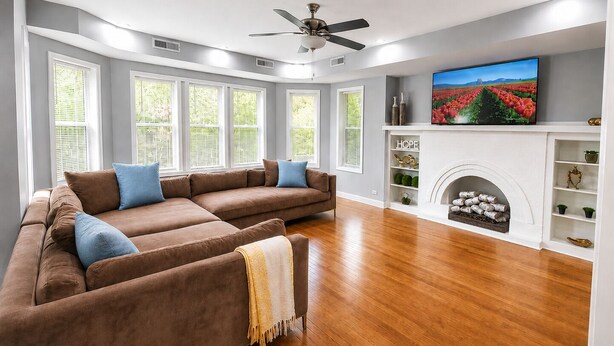 Una sala de estar con sofá modular, chimenea, televisión y ventilador de techo.