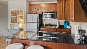 Une cuisine avec des meubles en bois, un réfrigérateur en acier inoxydable, un four à micro-ondes, un évier et deux tabourets.