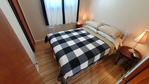 Ein Hotelzimmer mit kariertem Bettbezug, einem Nachttisch mit Lampe und einem Fenster mit Vorhängen.