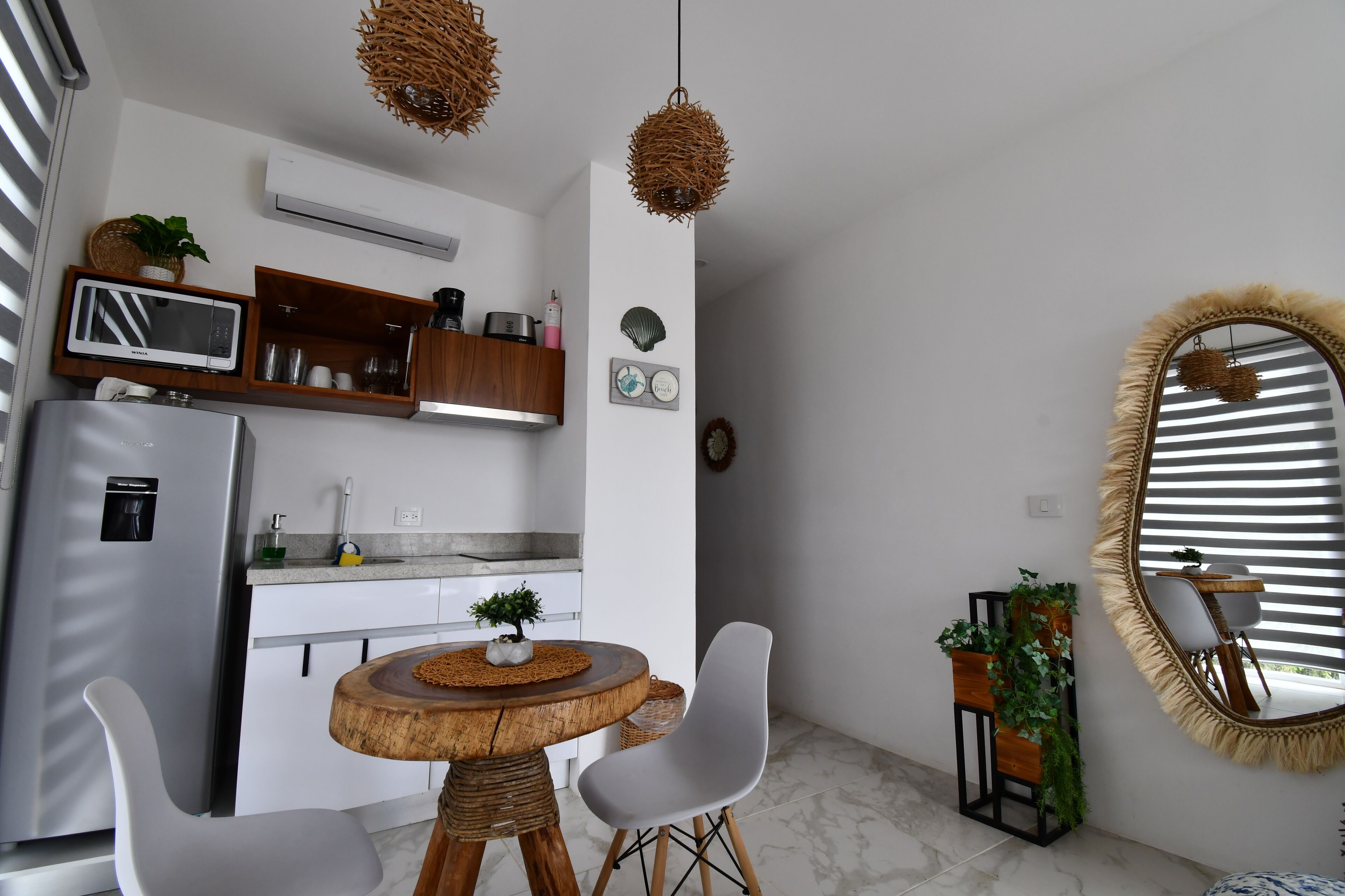 A compact kitchen with modern appliances, a dining area with a round wooden table, and a mirror with a fringe frame.