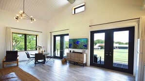 Ein geräumiges Wohnzimmer mit großem Fernseher, Holzboden und Blick ins Freie durch große Schiebetüren.