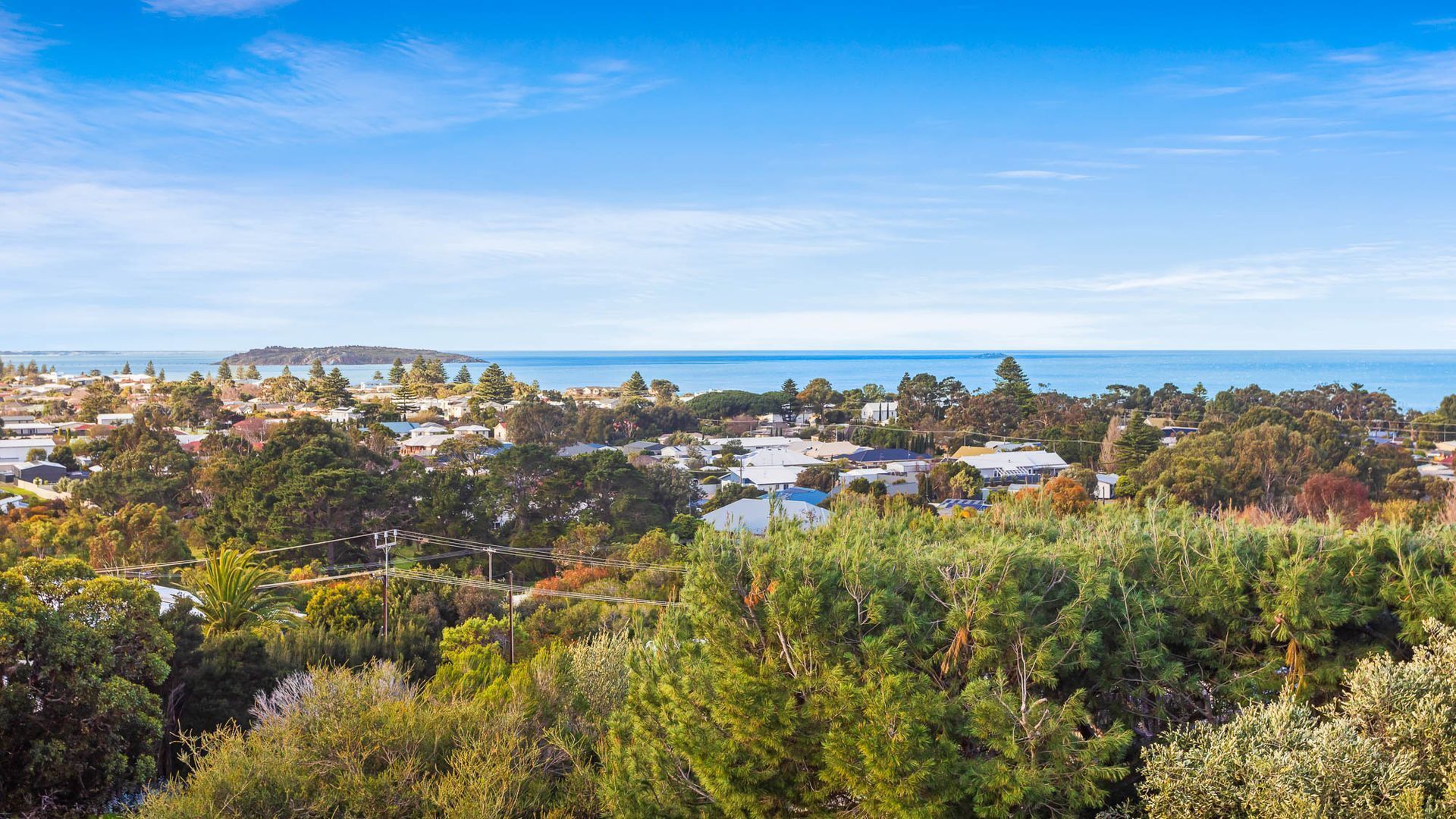 A coastal town with residential houses, dense greenery, and a view of the sea.