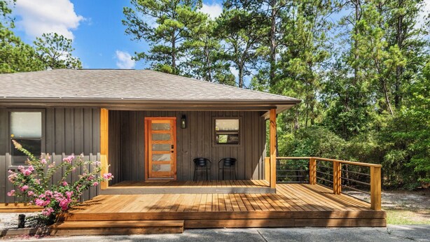 Una cabaña con terraza de madera, dos sillas y una puerta con panel de vidrio.