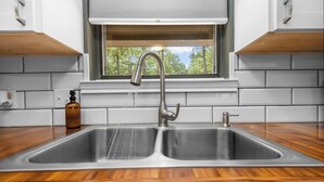 Una cocina con un lavaplatos doble de acero inoxidable, un ventanal con vistas a árboles y una encimera de madera.