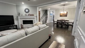 A living room with a sofa, TV, fireplace, dining area, and staircase.