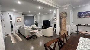 A modern living room with a sofa, TV, and fireplace. There is a dining table with chairs.