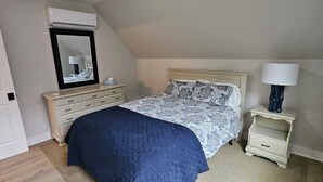 Une chambre à coucher avec un lit, une table de chevet, une lampe, un miroir et un luminaire au plafond.