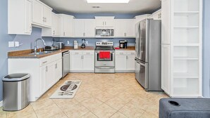 A modern kitchen with white cabinets, stainless steel appliances, and a tiled floor.