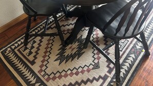 Ein runder Holzesstisch mit Glasplatte in der Mitte, umgeben von vier schwarzen Stühlen.