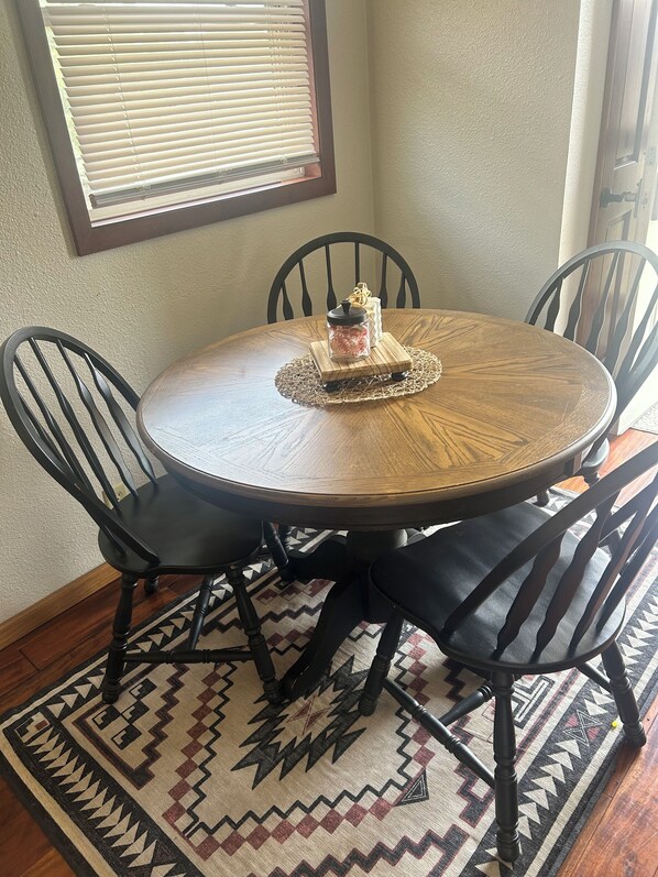 A round wooden dining table with a glass-top centerpiece, surrounded by four black chairs.
