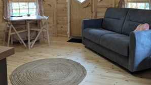 A cozy wooden interior with a dining table, a gray sofa, and a woven rug. - Kota Finlandais Deux Extensions Pour 4 Personnes, Tout Confort (Vignot)