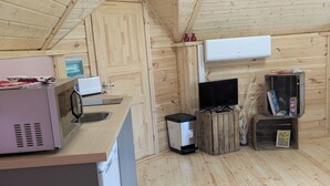 A compact kitchen with wooden walls and a sloped ceiling. It includes a microwave, a toaster, a sink, and a small refrigerator. - Kota Finlandais Deux Extensions Pour 4 Personnes, Tout Confort (Vignot)
