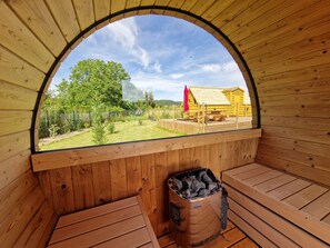 A wooden sauna with a curved roof, a bench, and a trash bin.