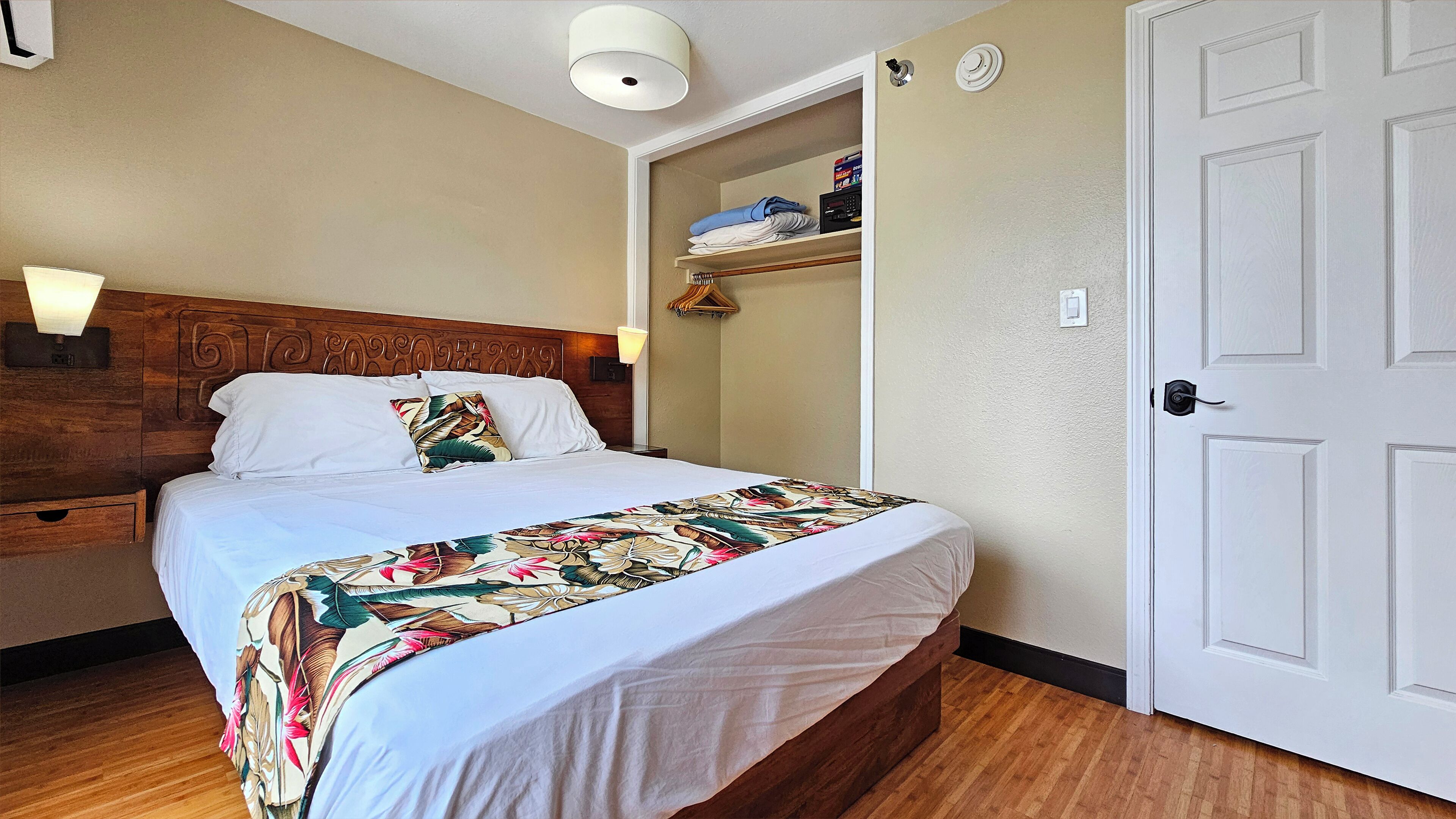 A neatly made bed with a floral bedspread, a wooden headboard, and a bedside lamp.