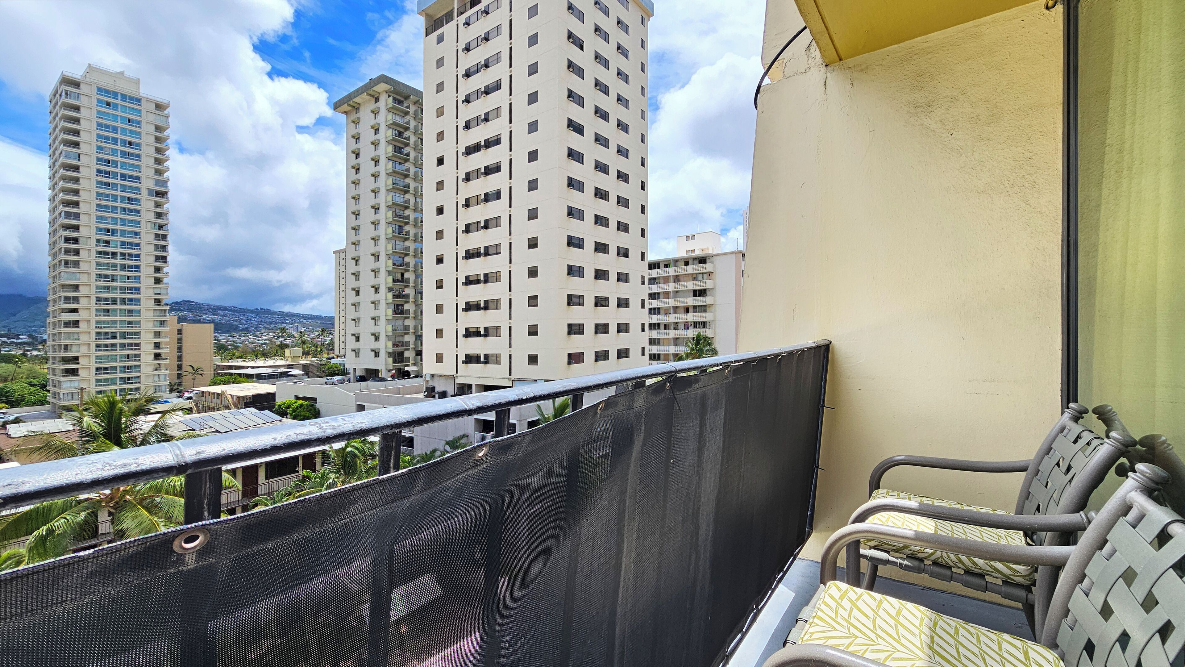 A balcony with a view of tall residential buildings, a mesh screen, and a chair.