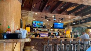 A rustic bar area with wooden stools, a bar counter, and ceiling fans.