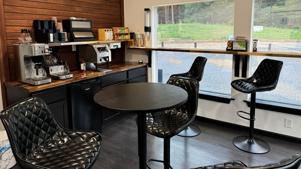 A modern cafe with a wooden wall, espresso machines, and black leather chairs. - Golden Pond Cabins (Altmar)
