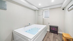 Une salle de bain avec une baignoire blanche, un petit tabouret en bois et un radiateur noir.