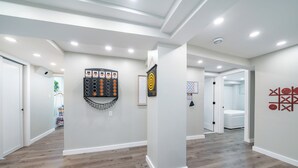 Un couloir moderne doté d’un plancher en bois, d’un éclairage encastré et de divers éléments de décoration murale, notamment un tableau encadré et un panneau de commande fixé au mur.