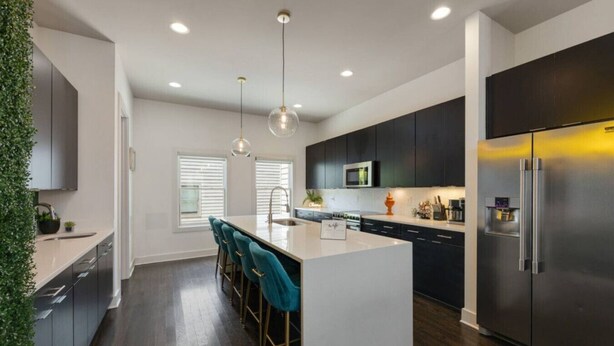 A modern kitchen with dark cabinets, a stainless steel refrigerator, a central island with bar stools, and pendant lighting. - Nashvilla Townhome- Gigantic Rooftop- Pure Luxury (Nashville)