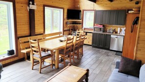 Interior de una cabaña de madera con comedor, cocina y sofá.