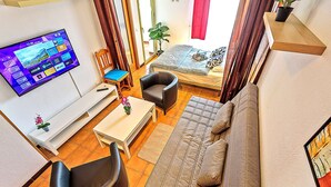 Una sala de estar con un sofá, sillas, una mesa de centro, un televisor y un balcón al que se accede por una puerta corredera.