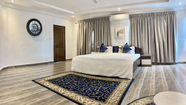 Une chambre d’hôtel avec un grand lit, un ventilateur de plafond, un appareil de climatisation, une petite table et un tapis décoratif.