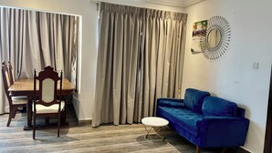 Un salon comprenant une table à manger, des chaises, un canapé bleu et un grand miroir rond accroché au mur.