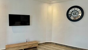Une chambre moderne dotée d’un téléviseur à écran plat fixé au mur, d’une console en bois et d’une horloge décorative.