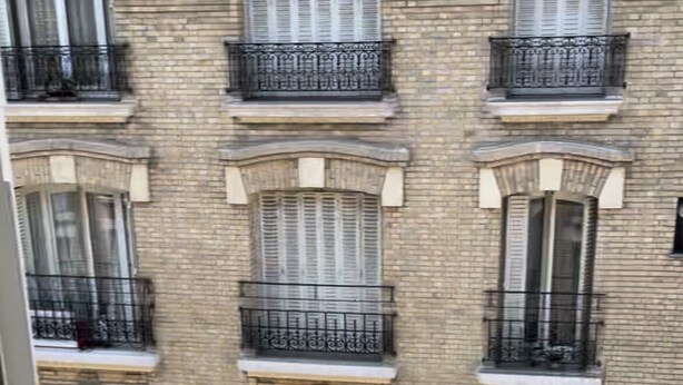 A multi-story building with a brick facade, multiple windows with shutters, and decorative iron railings on balconies.