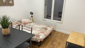 A compact room with a bed, a small table, a chair, and a potted plant.