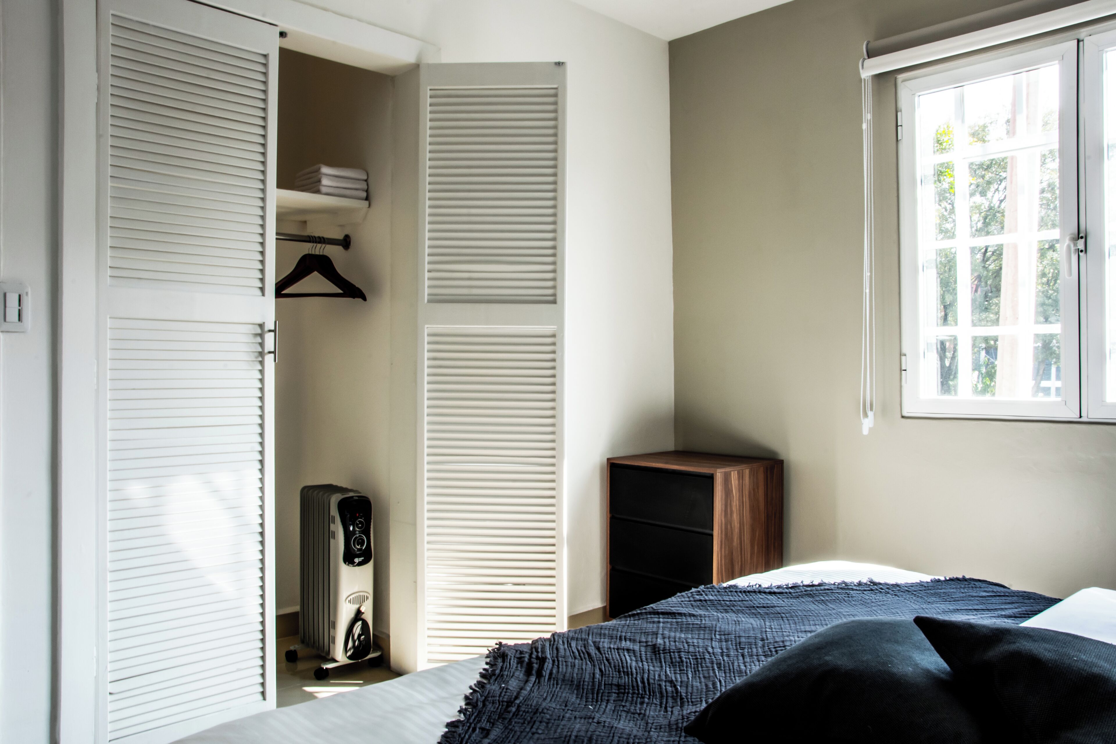 A bedroom with a bed, a radiator, a wardrobe, and a window.