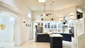 A spacious kitchen with white cabinets, a central island, and pendant lighting. - Spacious & Modern Pāhoa Retreat Near Kehena Beach! (Pahoa)