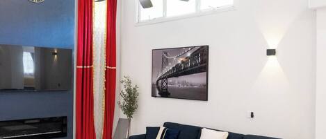 A modern living room with a sectional sofa, a flat-screen TV, a ceiling fan, and a large window.