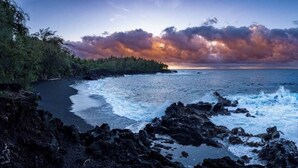 A coastal landscape with a rocky shoreline, waves crashing onto the beach, and a sunset in the background. - Spacious & Modern Pāhoa Retreat Near Kehena Beach! (Pahoa)