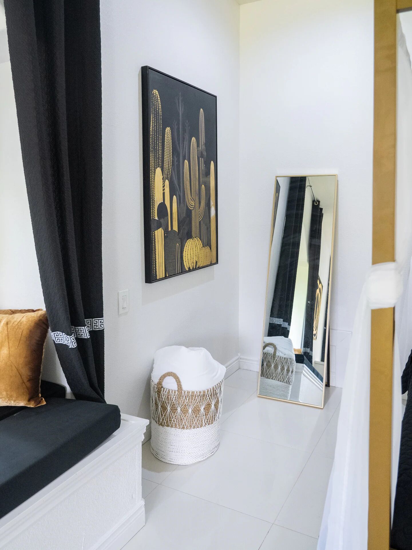 A modern living room with a black and white sofa, a white woven ottoman, a black and white artwork on the wall, and a large mirror reflecting the room.