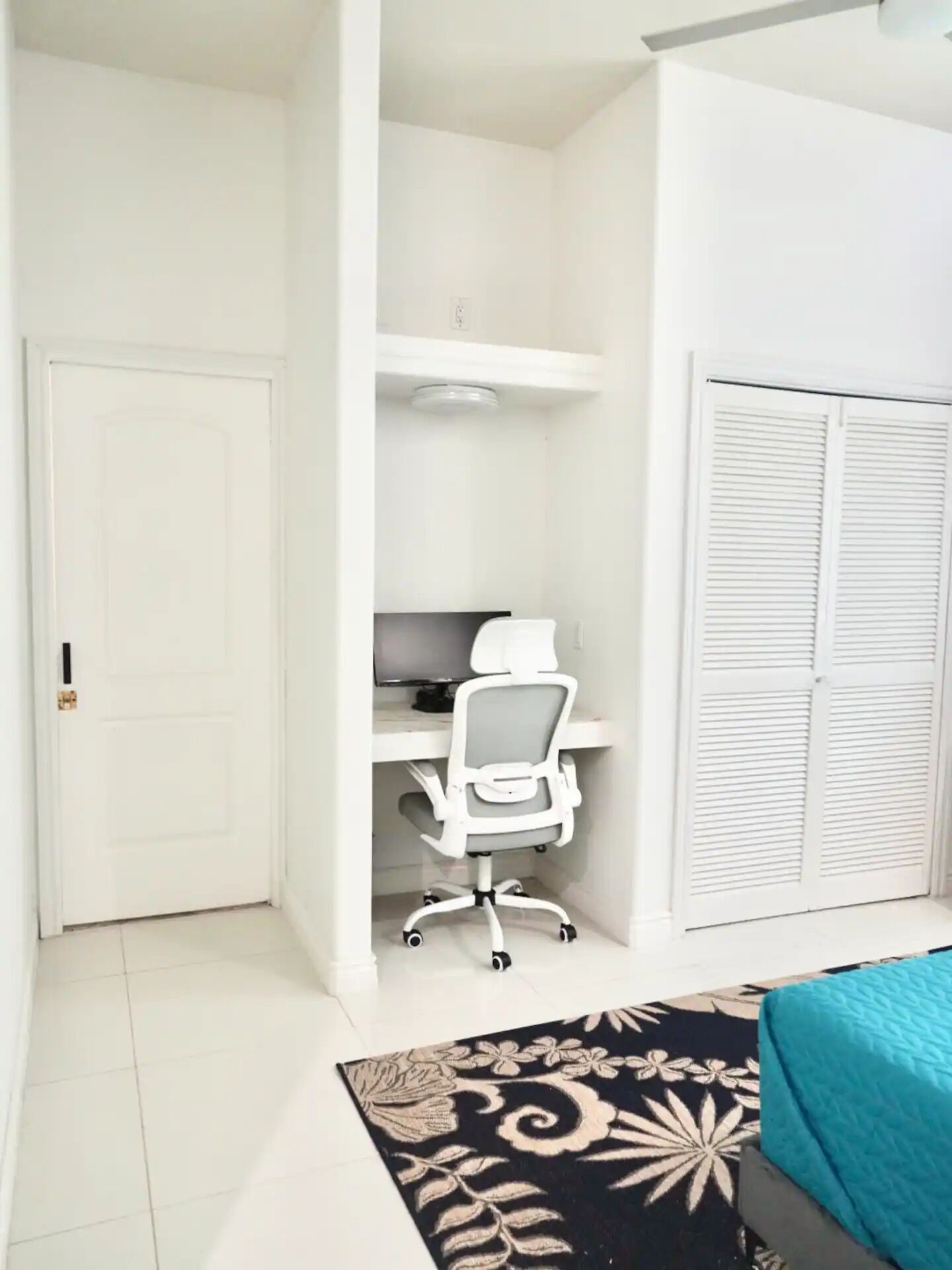 A bedroom with a bed, a desk with a chair, a wardrobe, and a patterned rug.