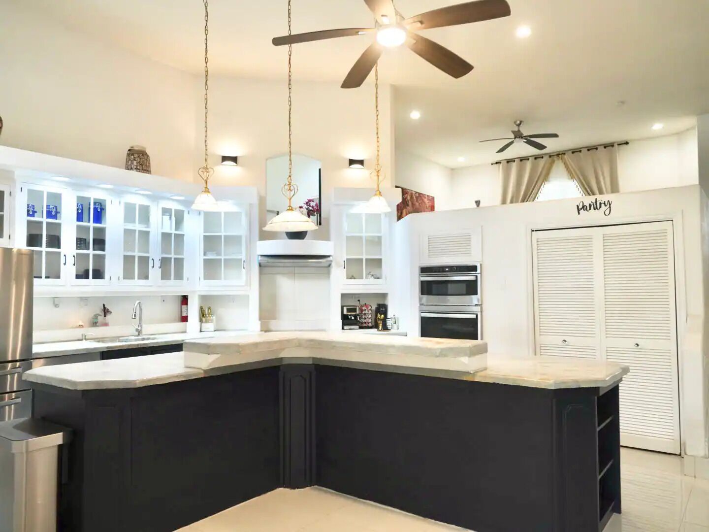 A modern kitchen with a central island, white cabinetry, and built-in ovens.