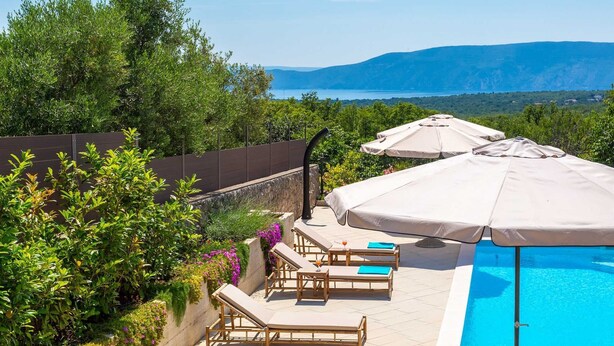 A poolside area with lounge chairs and umbrellas, surrounded by greenery and overlooking a body of water with mountains in the distance. - Villa Loni with Pool & Seaview (Bajčići (Krk))
