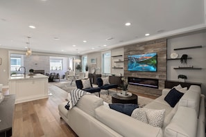 Uma sala de estar moderna com um sofá branco, uma TV na parede e uma lareira.