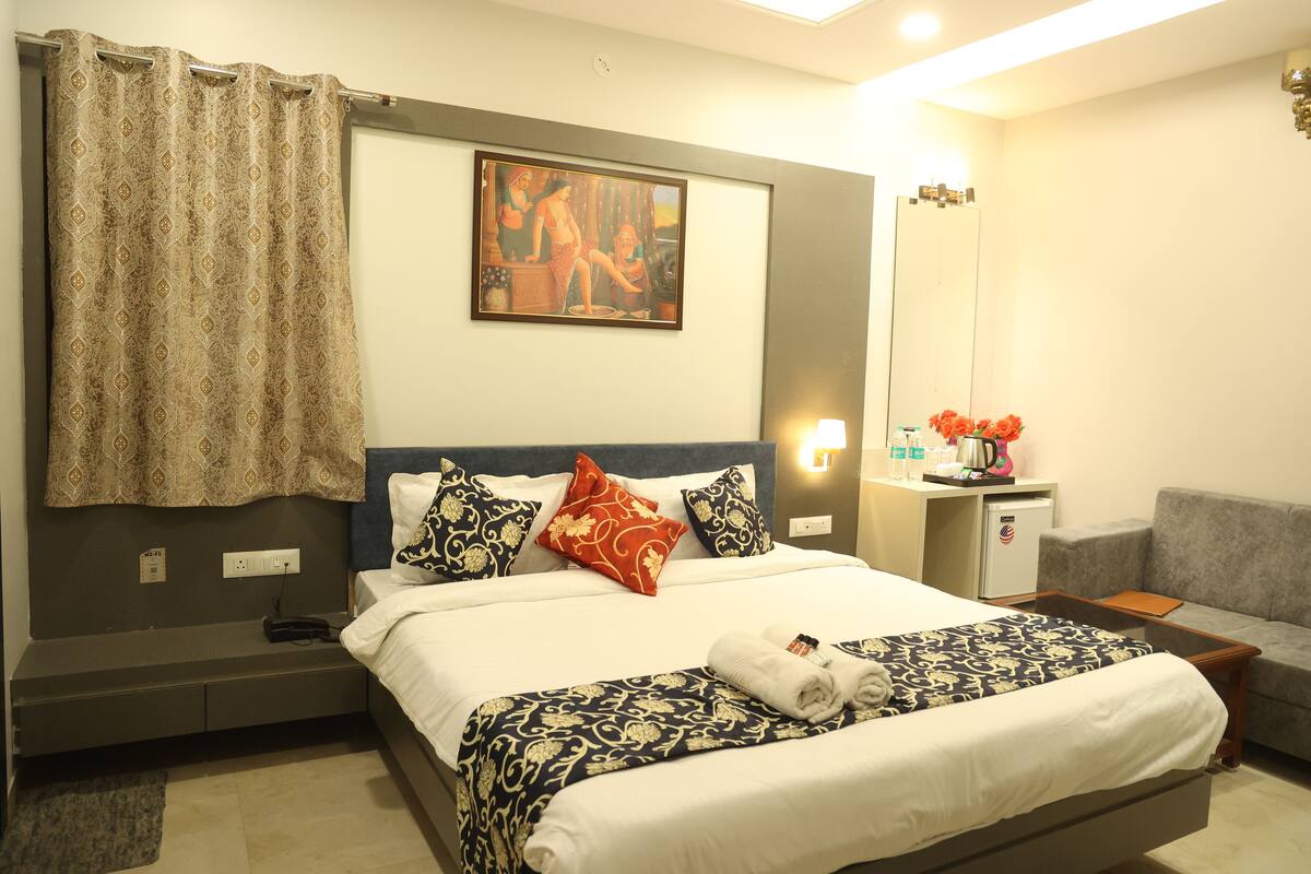 A hotel room with a bed, a desk, a chair, a mirror, and a painting on the wall.